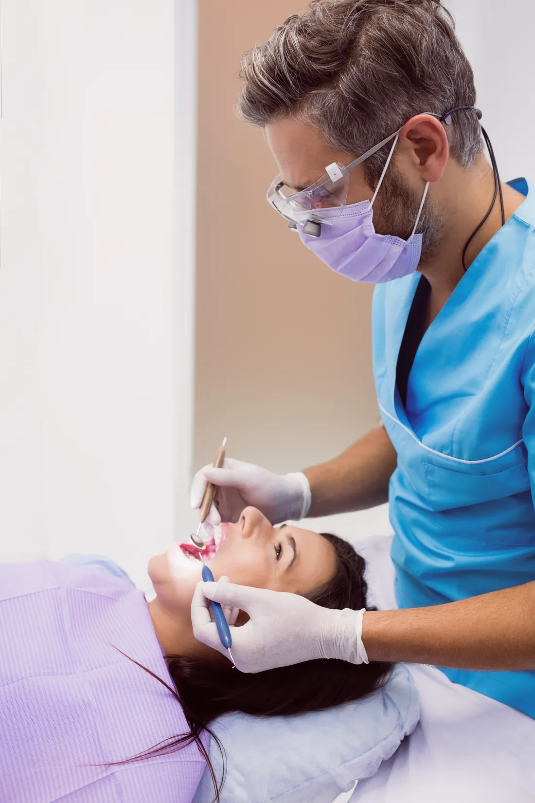 A dentist in a mask and gloves working on a patient with dental tools.